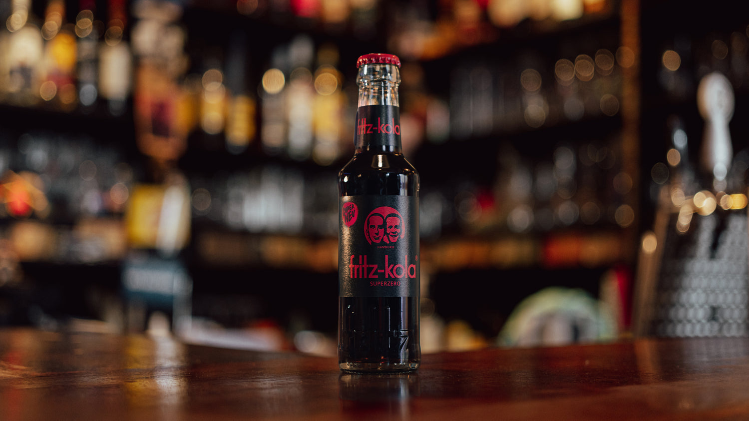 fritz-kola glasflasche steht auf einem holztresen in einer bar, unscharfe flaschen und gläser im hintergrund