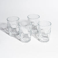 Vier leere fritz-kola Gläser auf weißem Hintergrund, fotografiert von oben. Die Gläser sind in quadratischer Anordnung platziert und zeigen deutlich die eingeprägten fritz-kola Schriftzüge. Klares Kristallglas mit charakteristischen Rillen und Prägungen wirft dezente Schatten.