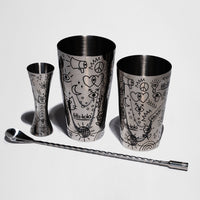 cocktailset mit zwei metallbechern, einem jigger und einem langen rührlöffel mit fritz-kola muster vor weißem hintergrund
