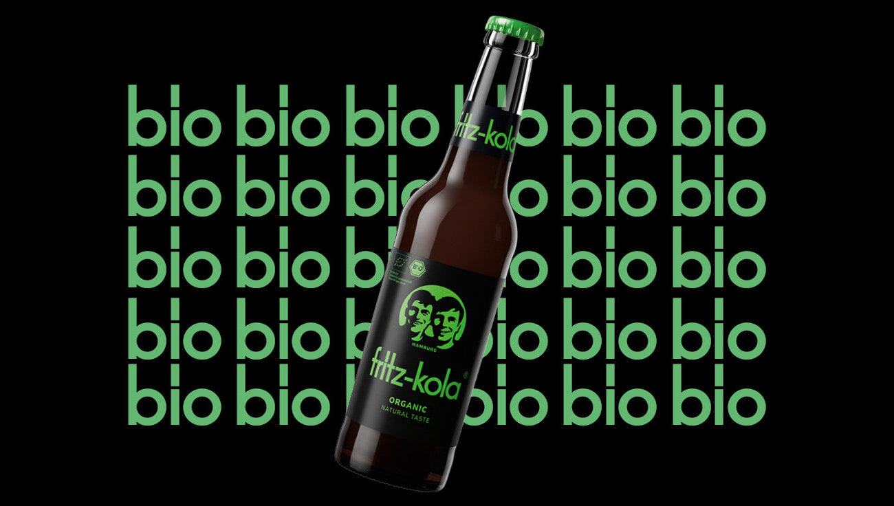 fritz-kola organic 0,33l Flasche ist vor einem schwarzen Hintergrund platziert, auf dem das Wort "bio" in grüner Schrift mehrfach wiederholt wird.