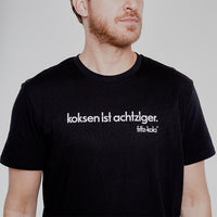 Mann trägt ein schwarzes Shirt mit dem Schriftzug "koksen ist achtziger. fritz-kola" in weiß auf der Brust