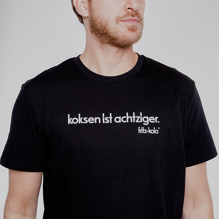 Mann trägt ein schwarzes Shirt mit dem Schriftzug "koksen ist achtziger. fritz-kola" in weiß auf der Brust