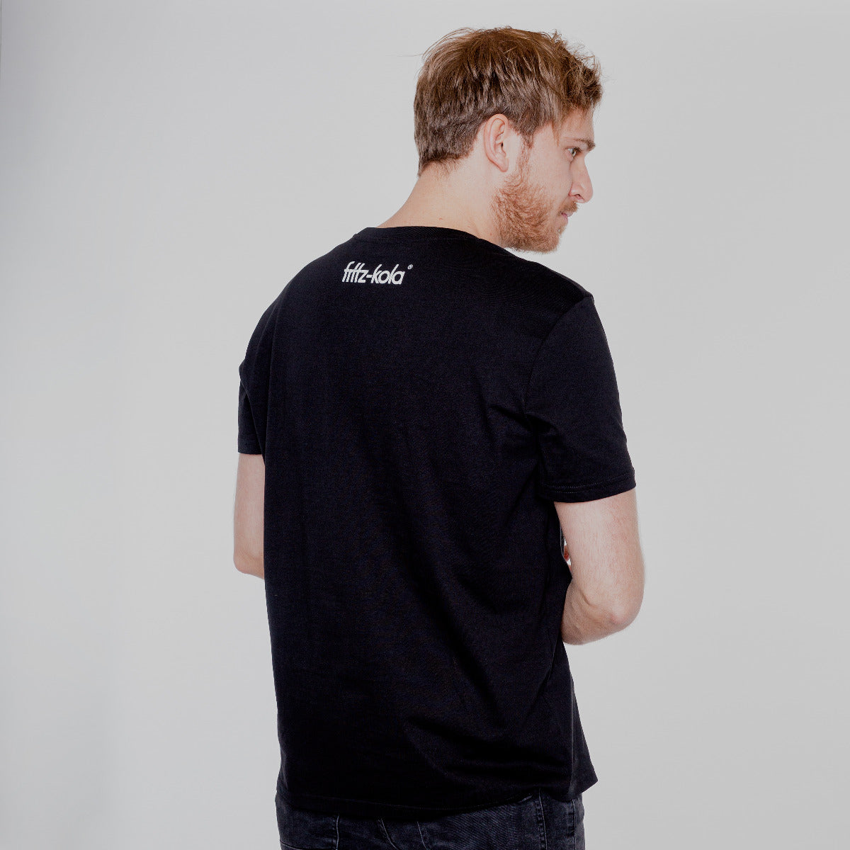 Junger Mann trägt schwarzes shirt mit weißem fritz-kola Schriftzug auf dem Nacken.
