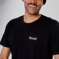 Nahaufnahme eines lächelnden Mannes in schwarzem T-Shirt mit kleinem weißem "fritz-kola" Schriftzug auf der Brust.