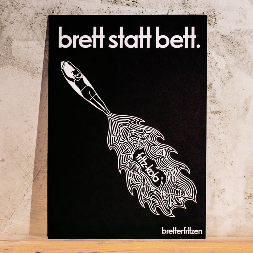 Schwarzes Kunstprint mit weißer Schrift "brett statt bett." oben und "bretterfritzen" unten. In der Mitte ein weißes Surfbrett, aus dem wellenartige Linien fließen, die an Wasser oder Wind erinnern. Das Print steht an einer wand