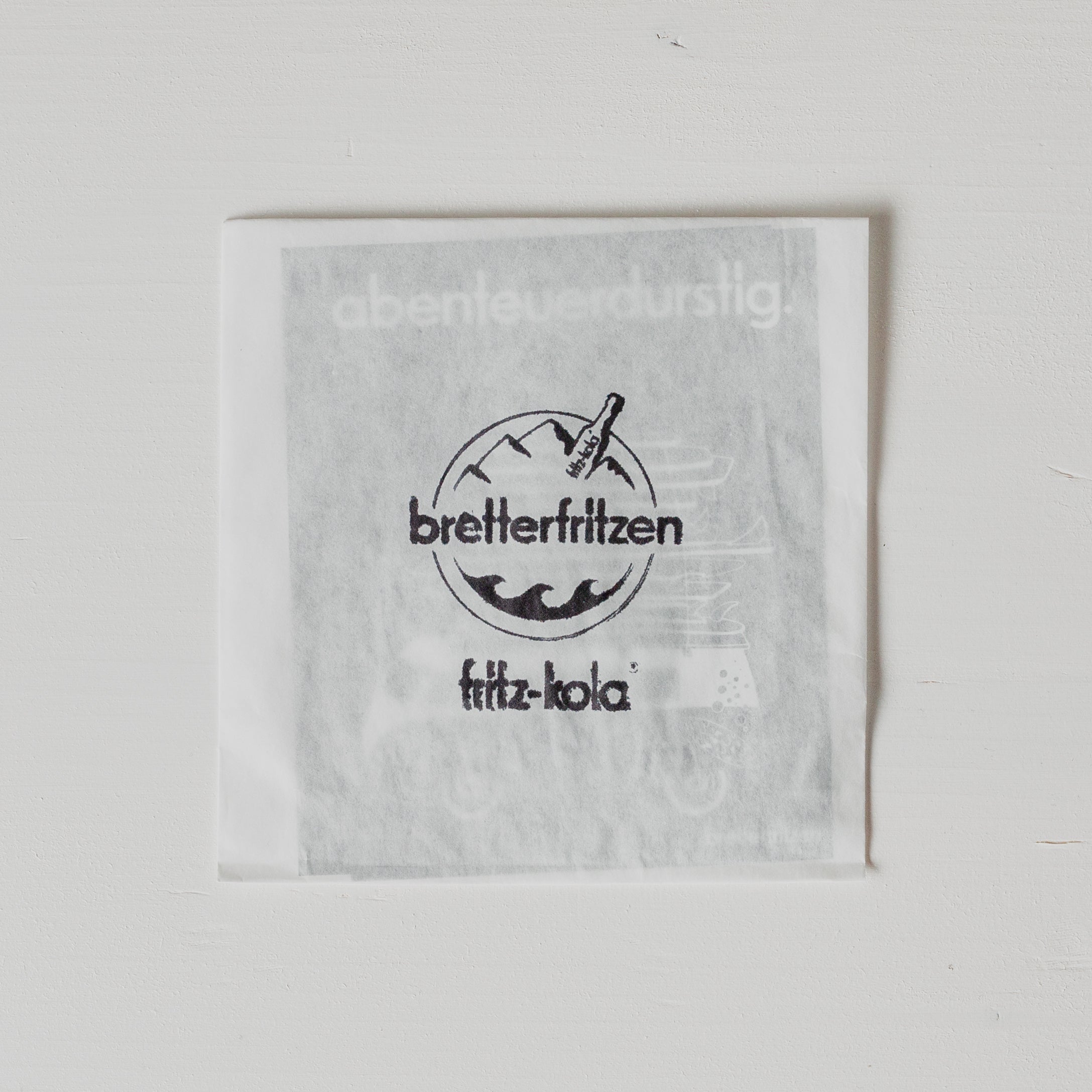 Weißer Briefumschlag mit durchscheinenden Stickern. Sichtbar ist "bretterfritzen" Logo mit Bergen und Wellen im Kreis, darunter "fritz-kola" Schriftzug in schwarzer Schrift.