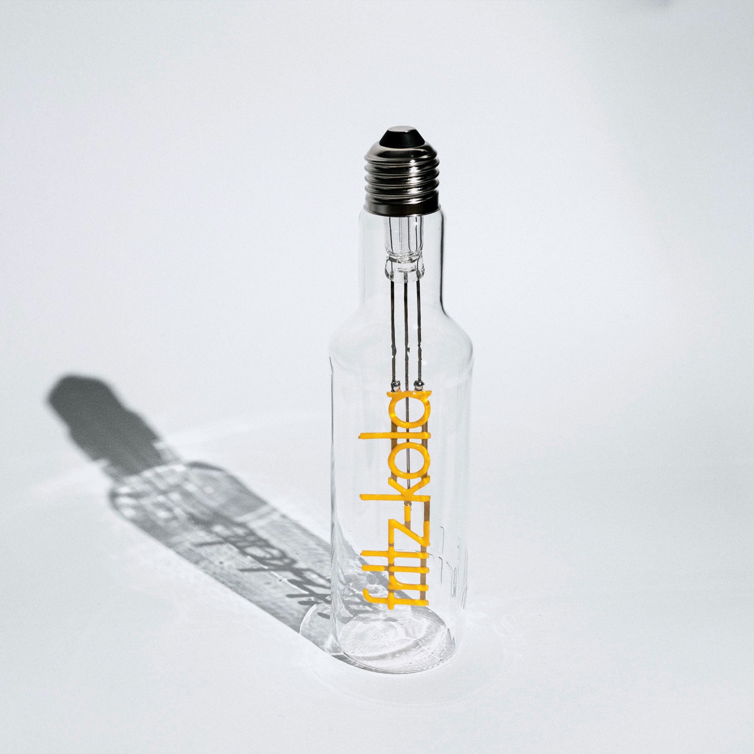 Glühbirne in Form einer fritz-kola Flasche mit Metallgewinde oben. Der Leuchtfaden ist in Form des fritz-kola Schriftzugs.