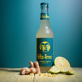 Auf einem Holztisch liegt ein Ingwer und eine Limette. In der Mitte der beiden ist die fritz-kola ingwer-limette Limonade im 0,33 Liter Gewinde zu sehen 