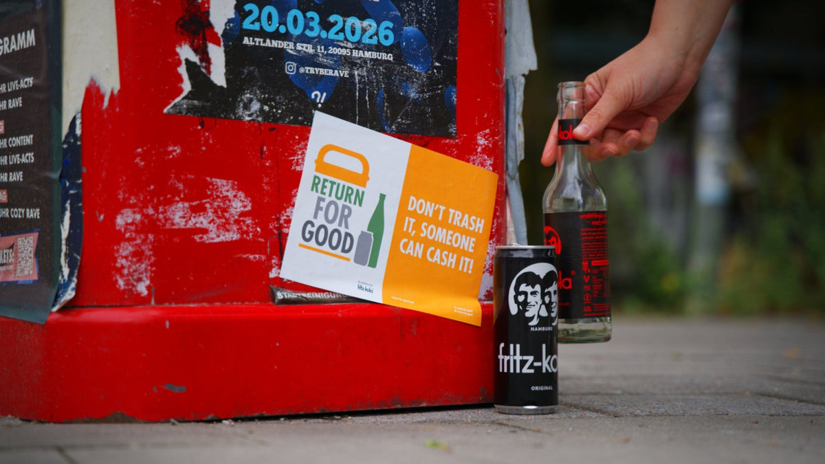 Naklejka Return For Good na czerwonym koszu na śmieci. Dłoń stawia obok niego butelkę fritz-koli.