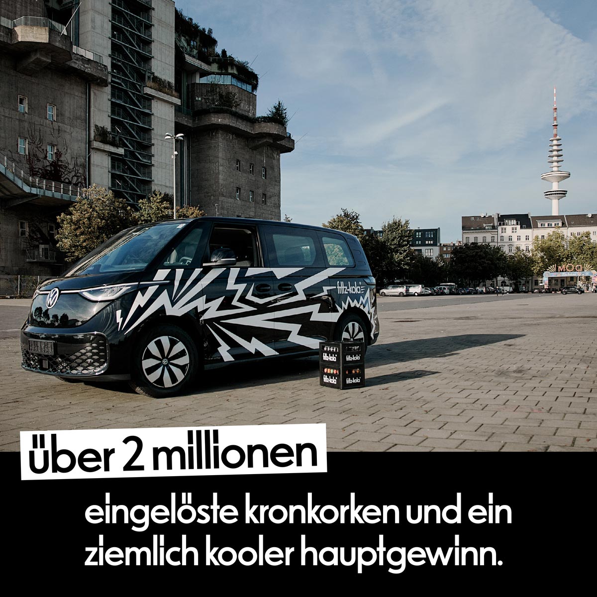 Schwarz-weiß gestalteter fritz-kola VW-Bus mit Getränkekisten auf einem Platz in Hamburg. Im Hintergrund sind der Hamburger Bunker und der Fernsehturm zu sehen. Im Bild steht: „Über 2 Millionen eingelöste Kronkorken und ein ziemlich kooler Hauptgewinn.