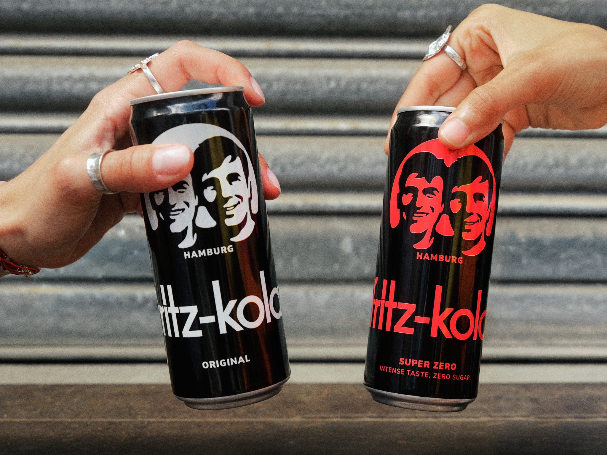 Nahaufnahme von den fritz-kola original und fritz-kola super zero Dosen. Die Dosen werden von zwei Personen gehalten die damit anstoßen. 