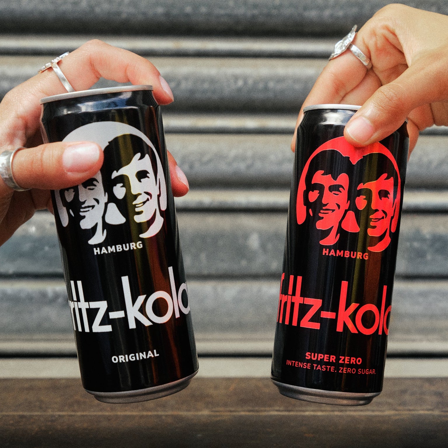 Nahaufnahme von den fritz-kola original und fritz-kola super zero Dosen. Die Dosen werden von zwei Personen gehalten die damit anstoßen. 