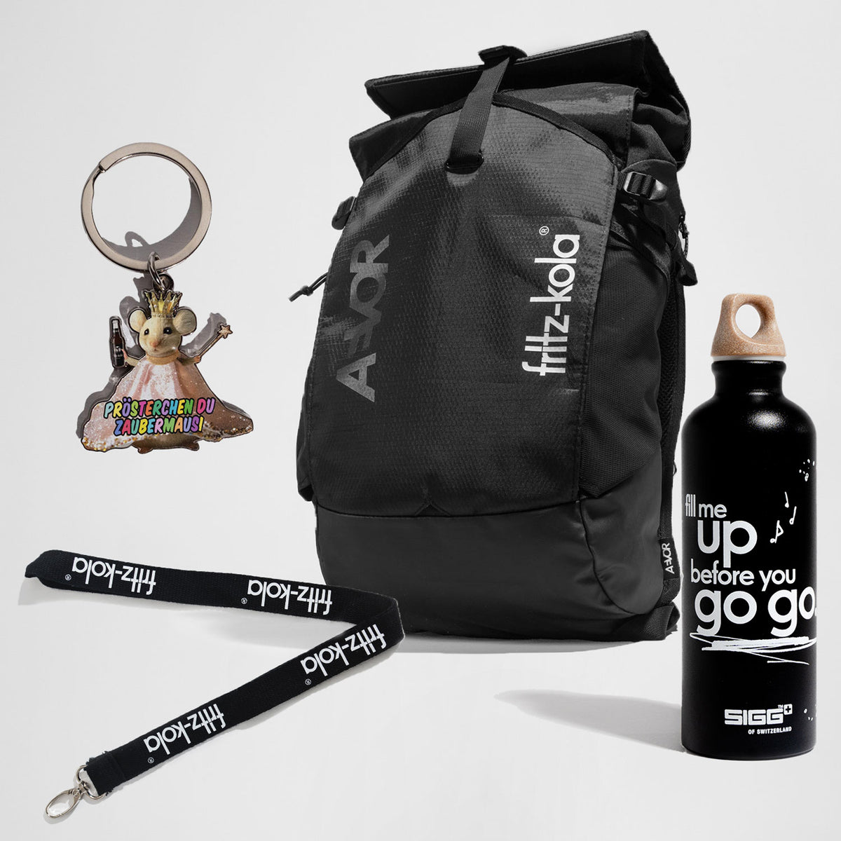 Set aus fritz-kola Merchandise: schwarzer AVOR-Rucksack mit fritz-kola-Logo, schwarze Trinkflasche mit weißem Schriftzug ‚fill me up before you go go‘, Schlüsselanhänger in Form einer Maus mit Krone und buntem Text ‚Prösterchen du Zaubermausi‘ sowie schwarzes Lanyard mit weißem fritz-kola-Schriftzug.