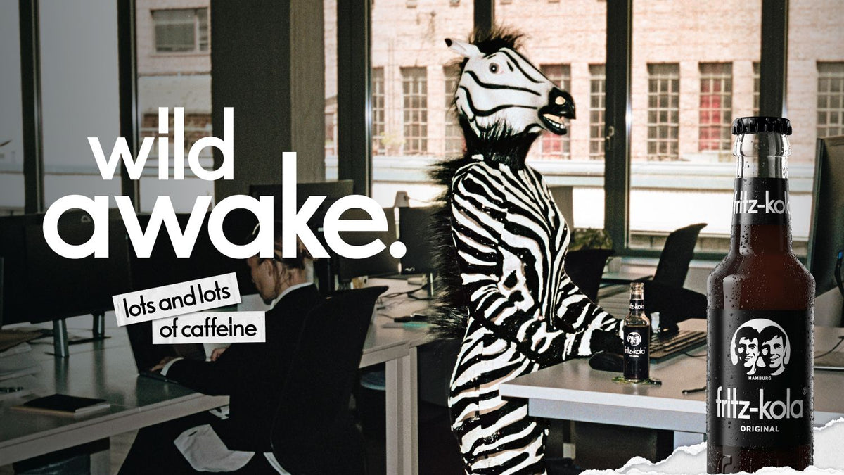 fritz-kola campaign featuring a person in a zebra costume in an office setting with the slogan “wild awake. lots and lots of caffeine”.